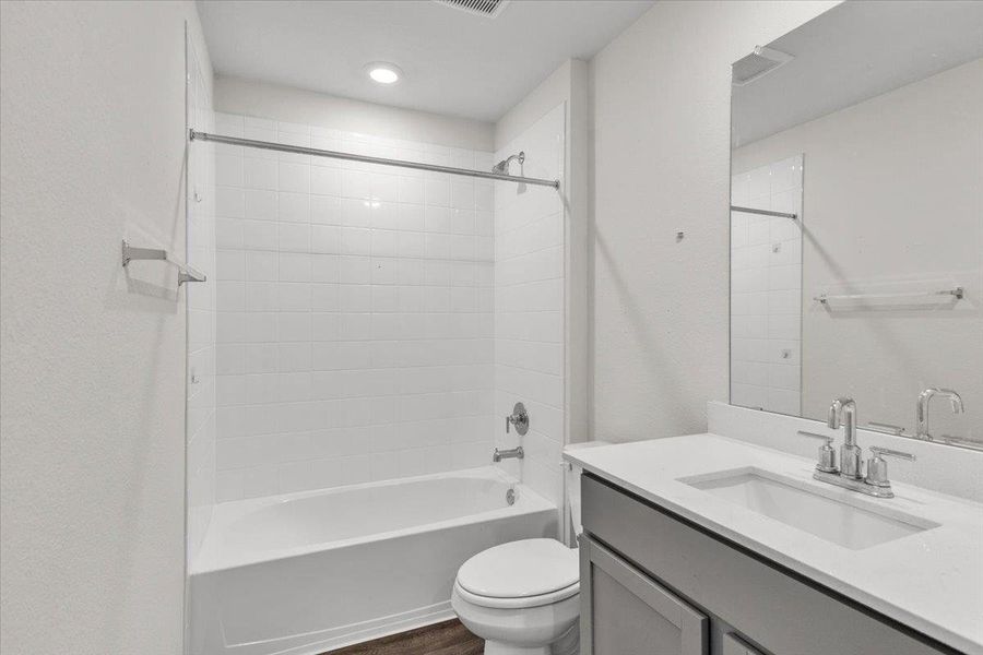 The bathroom features a white tub and shower combination with subway tile surround, a toilet, and a vanity with a white countertop and rectangular sink
