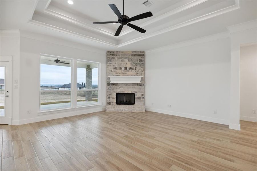 Unfurnished living room featuring a tray ceiling, light wood-type flooring, ceiling fan, and a large fireplace