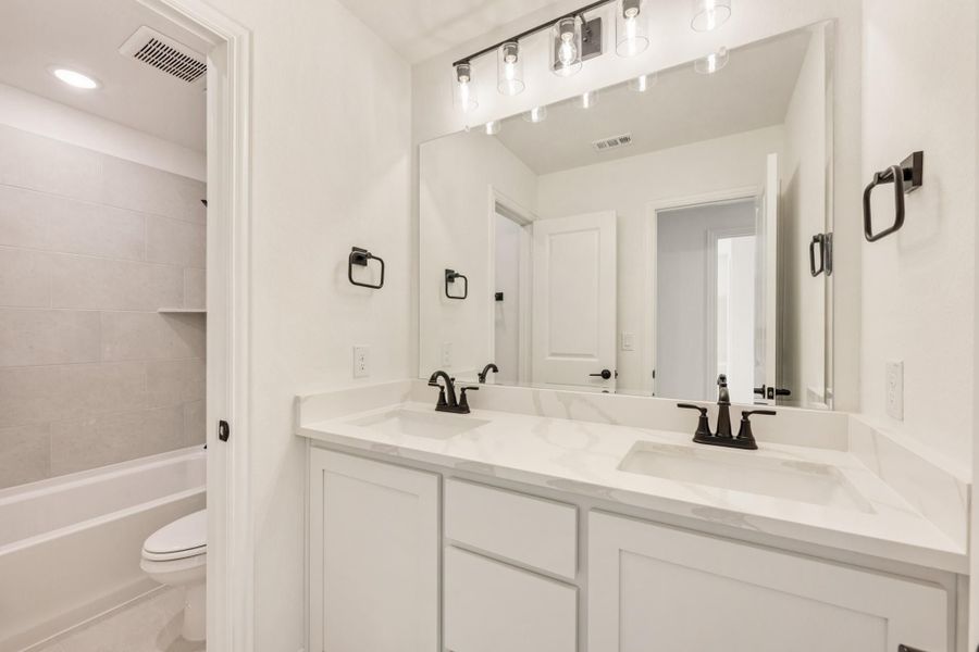 Bathroom with double sink vanity, white cabinets, quartz countertop, and tiled shower-tub combo