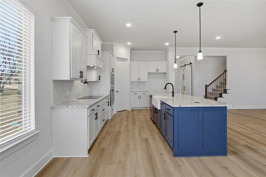 Two tone kitchen featuring a barn door, two tone cabinets, light stone counters, tasteful backsplash, and hanging light fixtures