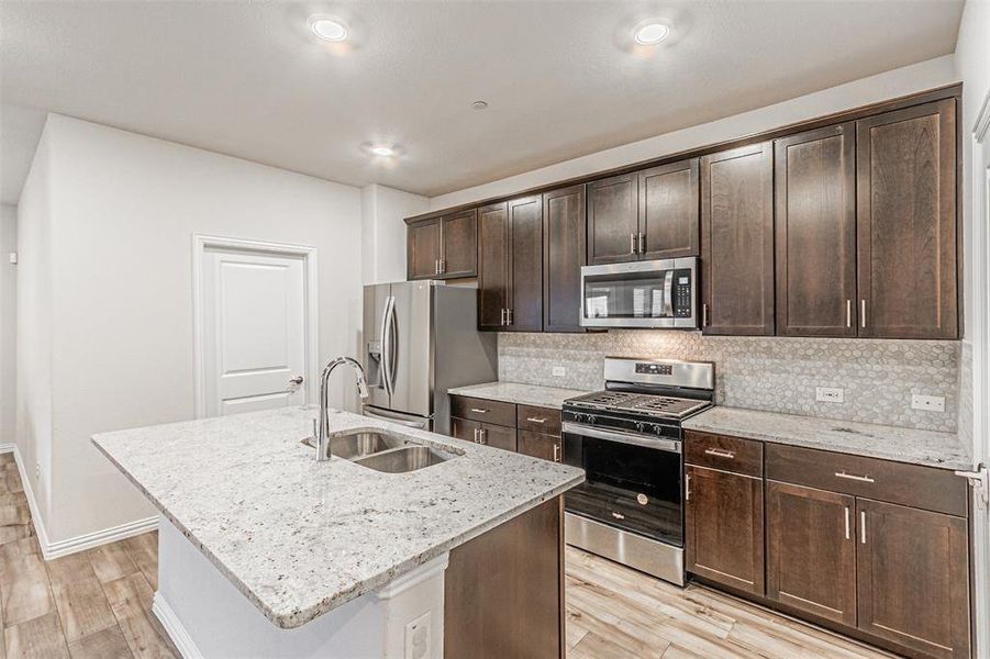 Kitchen featuring light wood finished floors, decorative backsplash, appliances with stainless steel finishes, and a sink