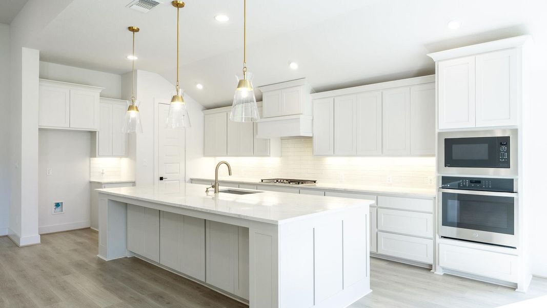 Kitchen with backsplash, stainless steel appliances, light wood-style flooring, a center island with sink, and lofted ceiling