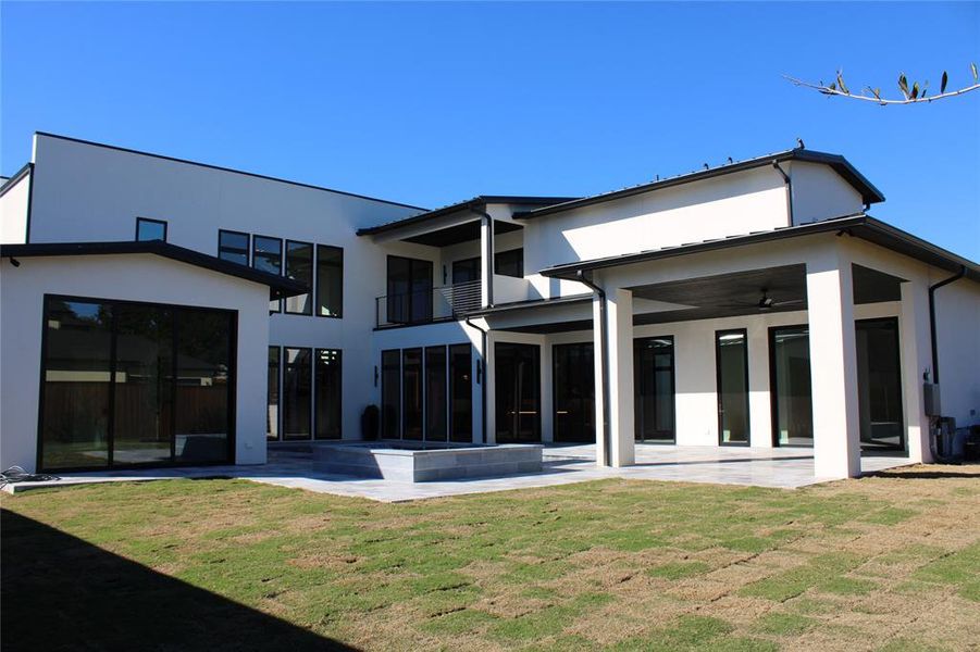 Back of property with ceiling fan, a patio area, and a lawn