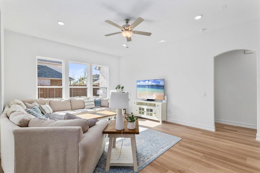 Bright living space featuring multiple windows, wood-finish flooring, recessed lighting, a ceiling fan, and an arched doorway