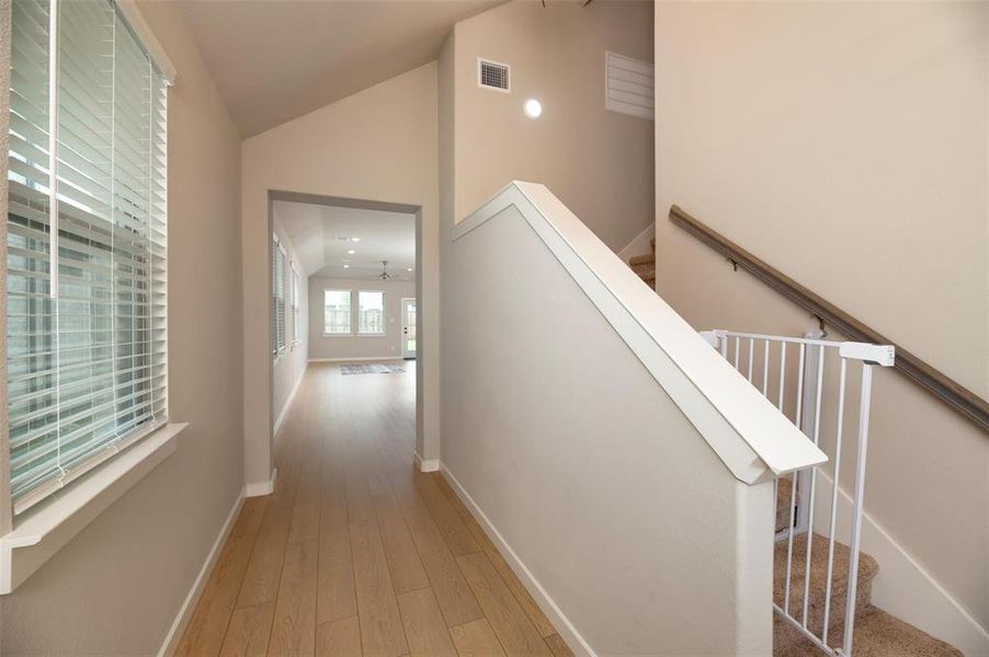Corridor with vaulted ceiling, light wood finished floors, stairway, and recessed lighting Corridor with vaulted ceiling, light wood finished floors, stairway, and recessed lighting