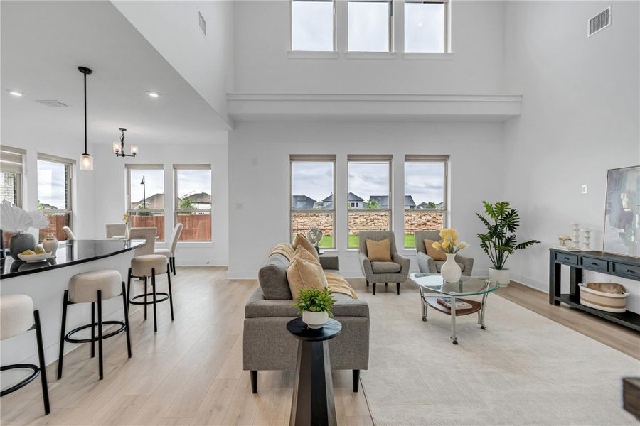 Natural light floods this spacious great room with soaring ceilings and light hardwood-style flooring.