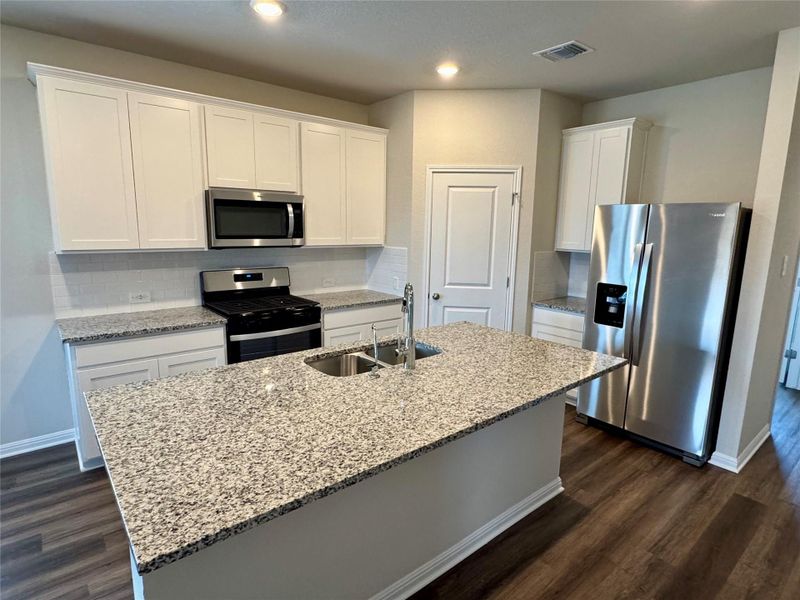 Kitchen with appliances with stainless steel finishes, white cabinets, dark wood-type flooring, a kitchen island with sink, and recessed lighting Kitchen with appliances with stainless steel finishes, white cabinets, dark wood-type flooring, a kitchen island with sink, and recessed lighting