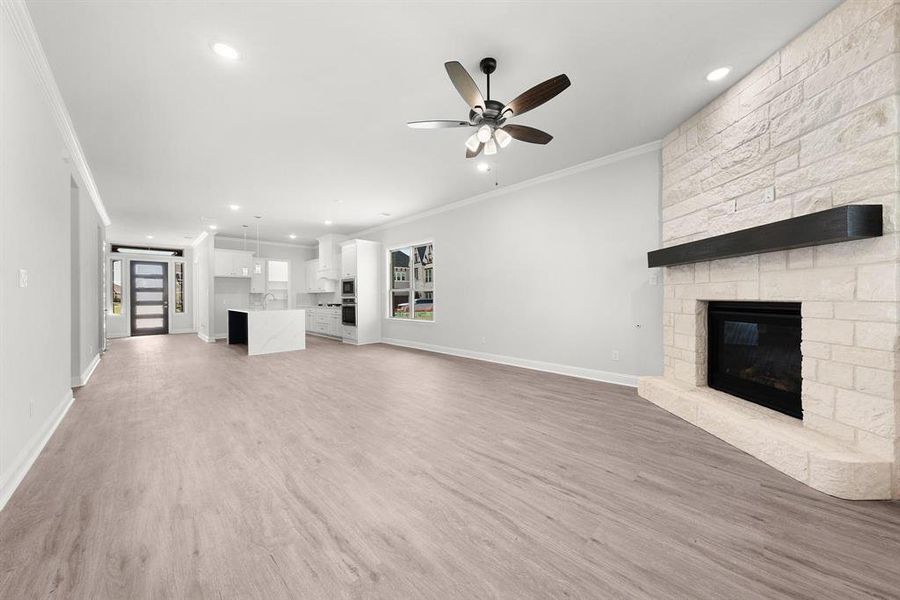 Large living room featuring an open floorplan, a gas fireplace, crown molding, luxury vinyl flooring, ceiling fan, and recessed lighting