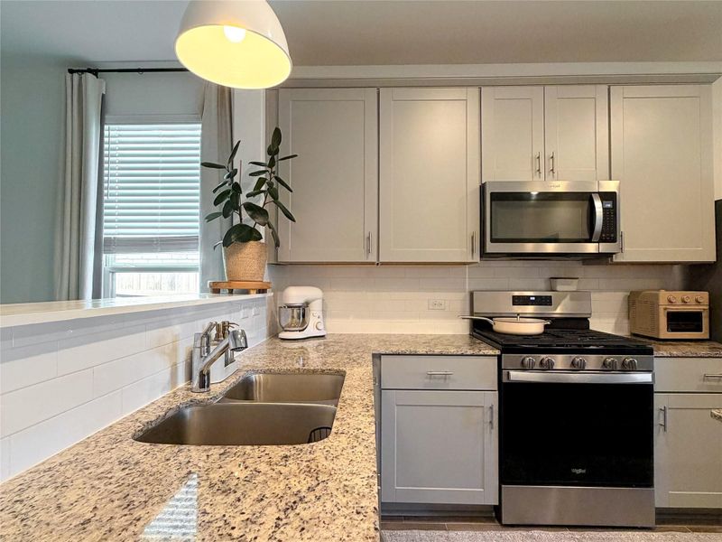 Kitchen with stainless steel appliances, backsplash, light stone countertops, gray cabinetry, and pendant lighting Kitchen with stainless steel appliances, backsplash, light stone countertops, gray cabinetry, and pendant lighting