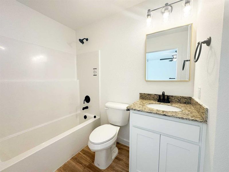 Bathroom featuring wood finished floors, vanity, baseboards, toilet, and shower / bathtub combination