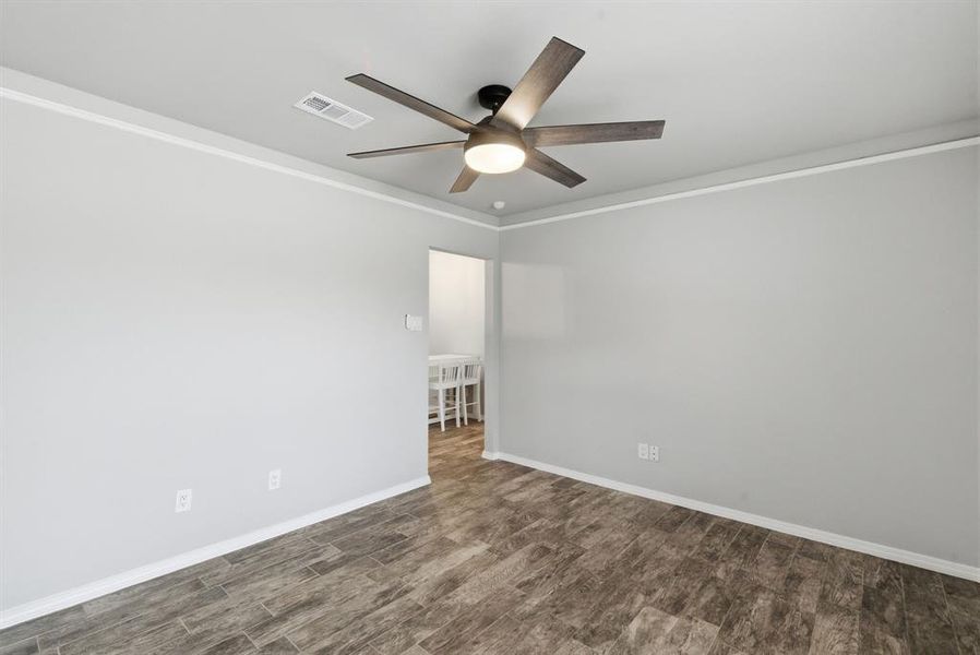 Empty room with ornamental molding, dark wood-style flooring, and a ceiling fan Empty room with ornamental molding, dark wood-style flooring, and a ceiling fan