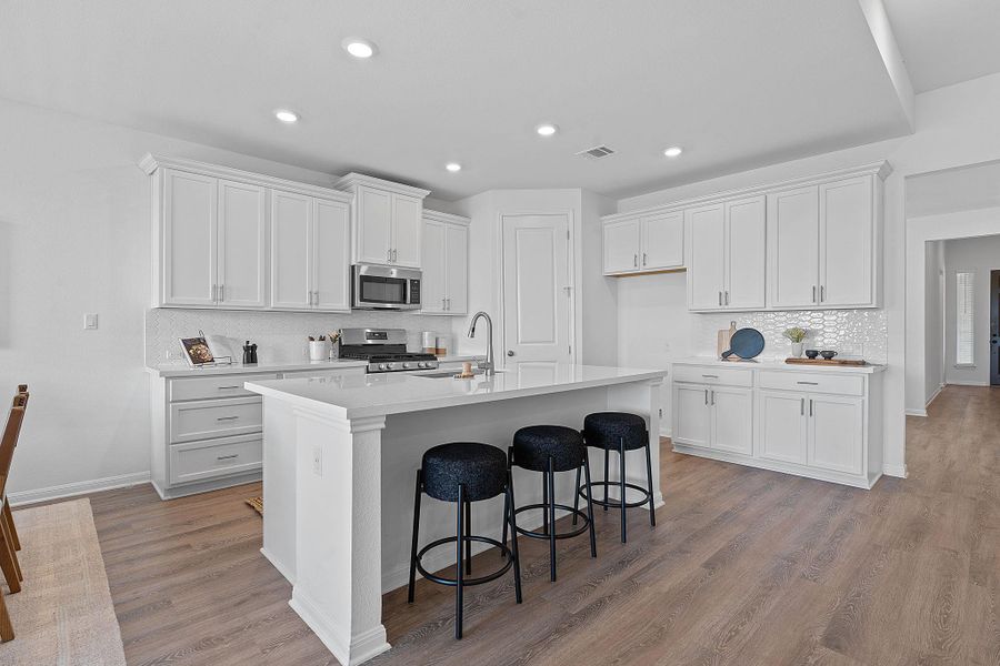 Kitchen featuring stainless steel appliances, decorative backsplash, an island with sink, white cabinets, and a kitchen bar