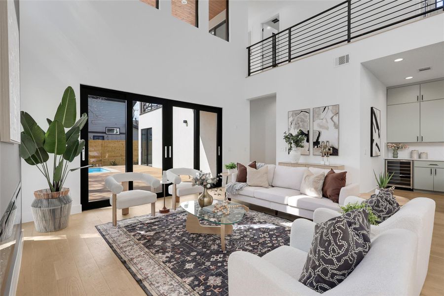 Living room with light wood finished floors, wine cooler, french doors, bar with sink, and a high ceiling