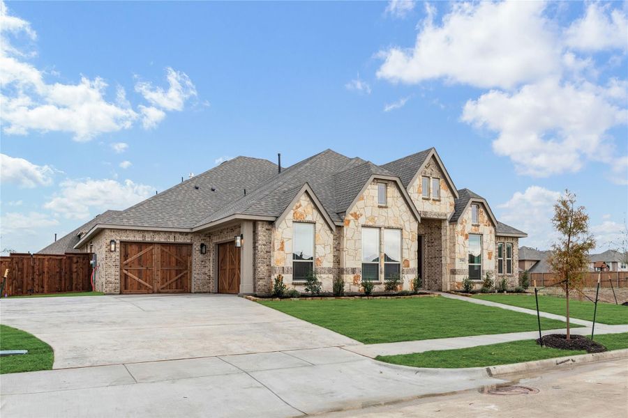 Single-story home with stone and brick exterior, two-car garage with wood doors, and green front lawn