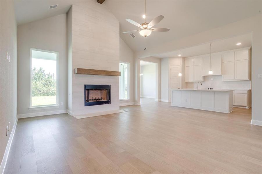 Unfurnished living room featuring ceiling fan, light hardwood / wood-style flooring, high vaulted ceiling, a tiled fireplace, and sink