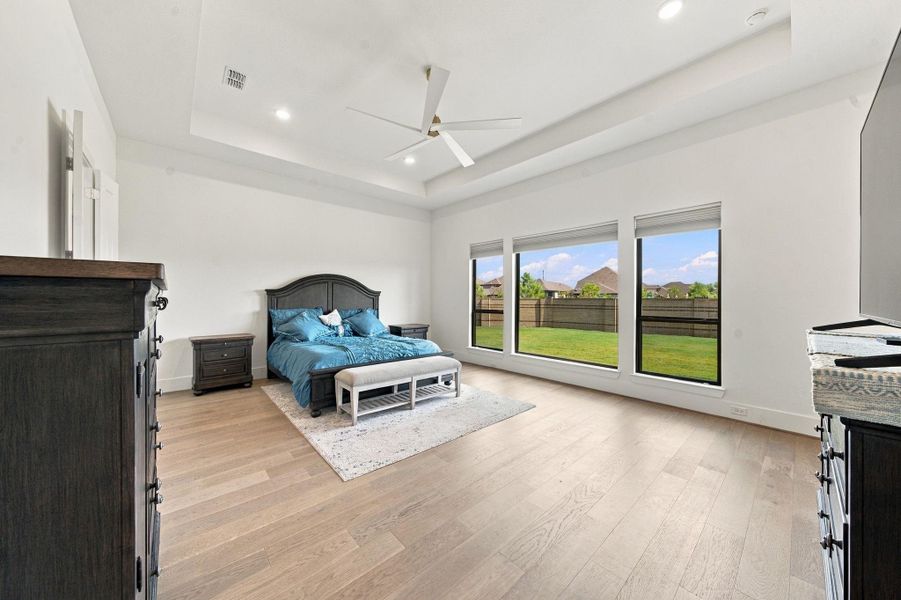 Wake up to backyard views in this spacious primary bedroom, featuring wood-look flooring, tray ceiling, and plenty of room for a full furniture set. Large windows bring in ample daylight while keeping the space private and serene.