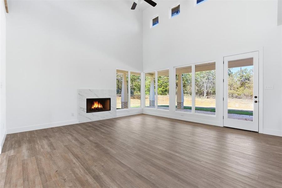 Unfurnished living room featuring a fireplace, a high ceiling, wood finished floors, and ceiling fan Unfurnished living room featuring a fireplace, a high ceiling, wood finished floors, and ceiling fan