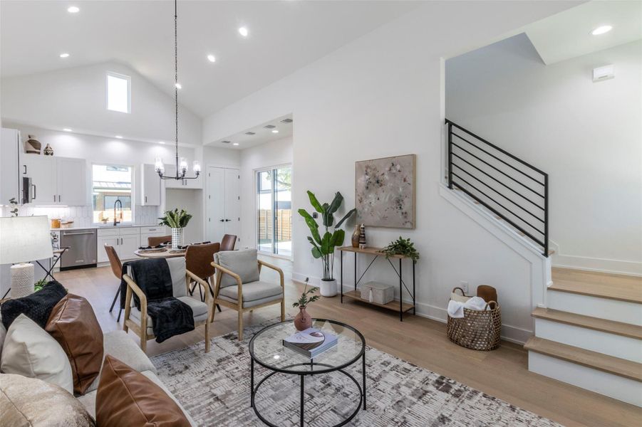 Living area with high vaulted ceiling, stairs, light wood-style floors, recessed lighting, and a chandelier