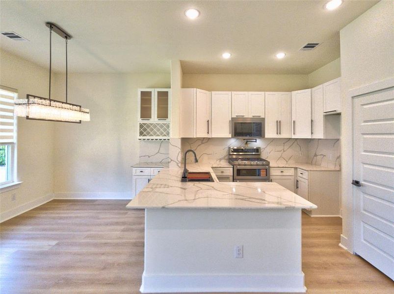 Open-concept kitchen featuring an island with a waterfall countertop, white cabinetry with dark hardware, stainless steel appliances, and wood-finish flooring