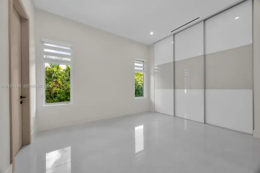 Polished tile flooring, floor-to-ceiling sliding glass-panel closet doors, and dual casement windows with integrated shades