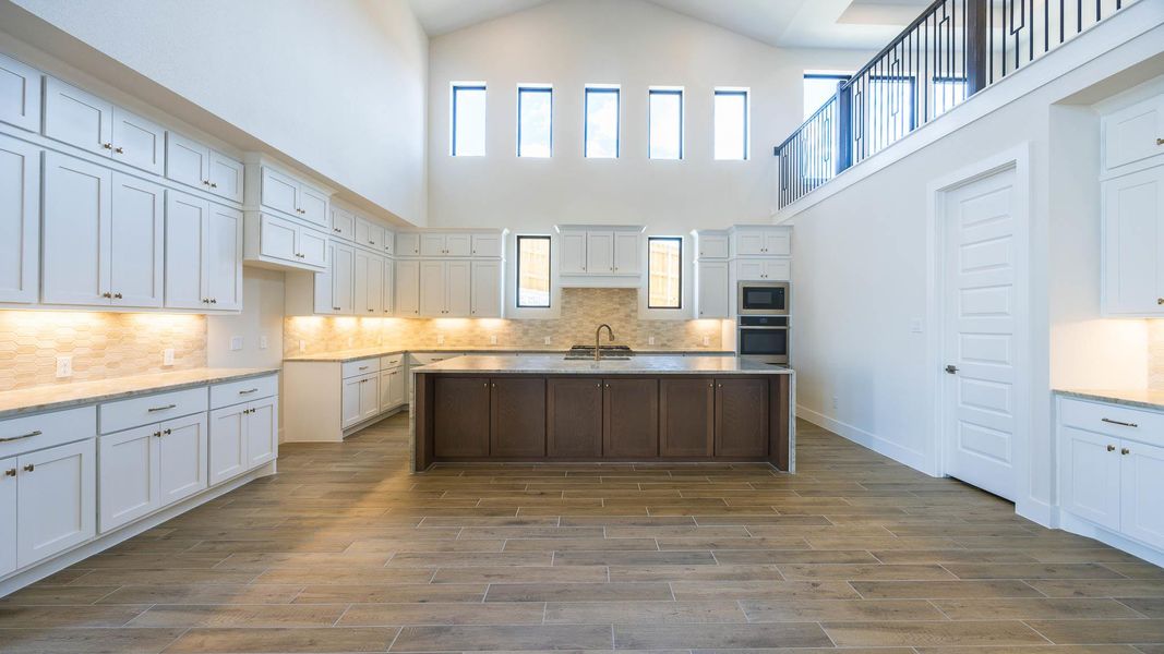 Kitchen with an island with sink, tasteful backsplash, white cabinetry, light stone counters, and a high ceiling Kitchen with an island with sink, tasteful backsplash, white cabinetry, light stone counters, and a high ceiling