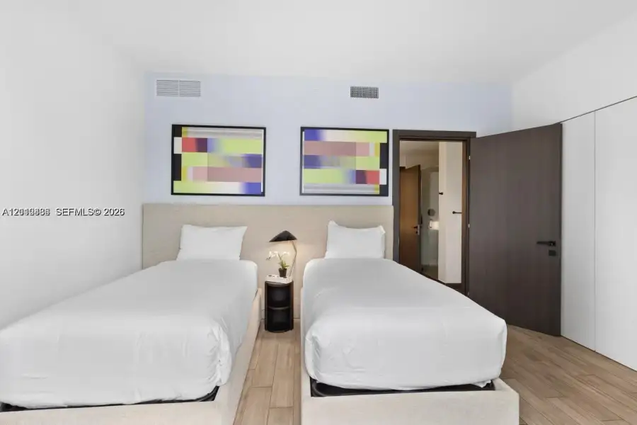 Neutral-toned upholstered headboard with integrated nightstand, wood-finish flooring, and dark-finished solid core swing door Neutral-toned upholstered headboard with integrated nightstand, wood-finish flooring, and dark-finished solid core swing door