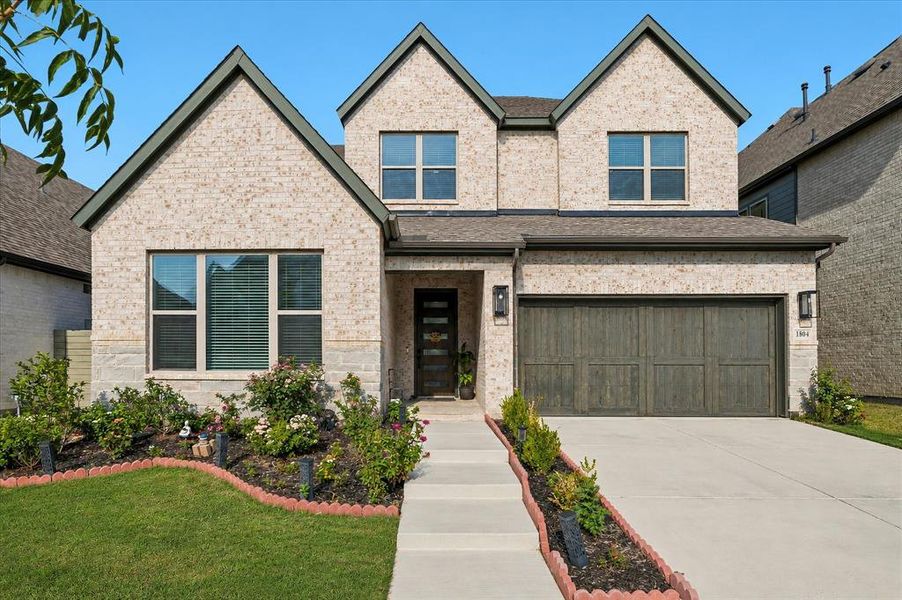 Contemporary two-story residence featuring light brick and stone veneer, multiple gables, and a dark wood-finish garage door Contemporary two-story residence featuring light brick and stone veneer, multiple gables, and a dark wood-finish garage door
