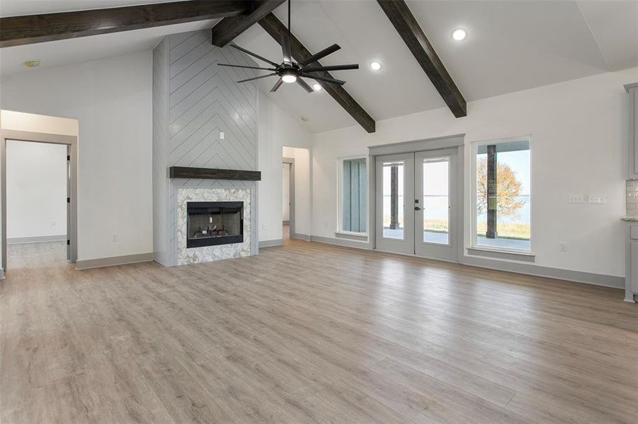 Unfurnished living room with high vaulted ceiling, ceiling fan, beam ceiling, a fireplace, and light hardwood / wood-style floors