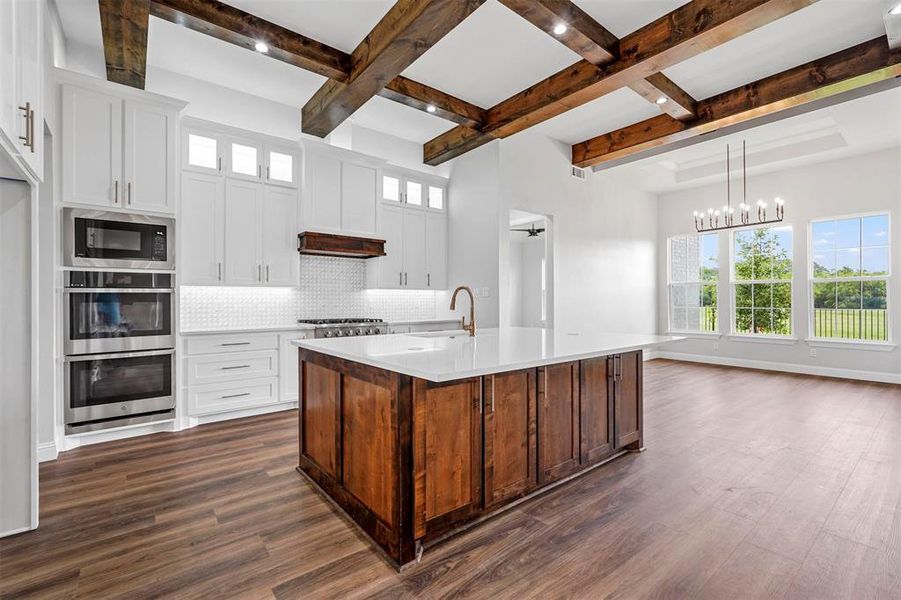 Kitchen with hanging light fixtures, black microwave, dark wood-type flooring, a kitchen island with sink, and tasteful backsplash