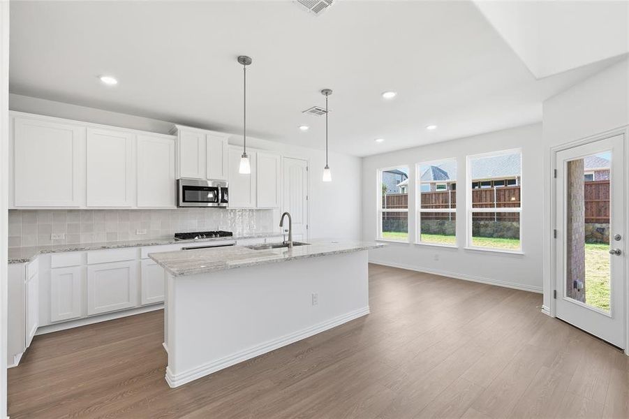 Kitchen with white cabinetry, a center island with sink, hanging light fixtures, light stone countertops, and recessed lighting