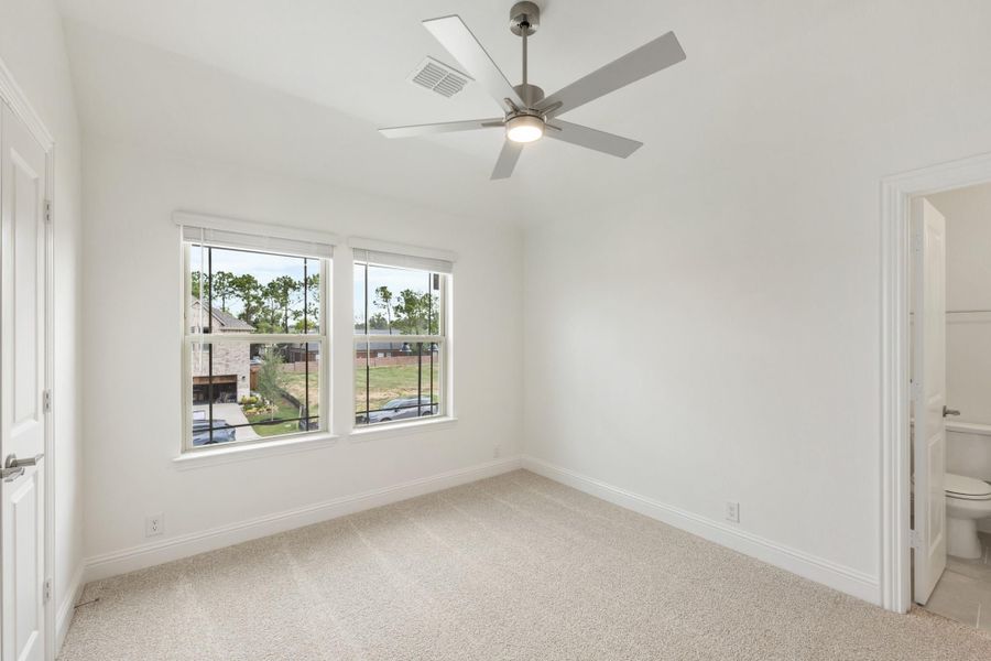 Empty bedroom with carpet, ceiling fan, two windows, and an attached bathroom doorway