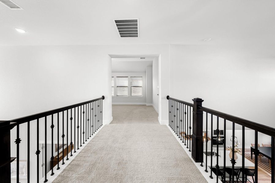 A well-lit second-story hallway with durable carpeting and elegant iron railings.