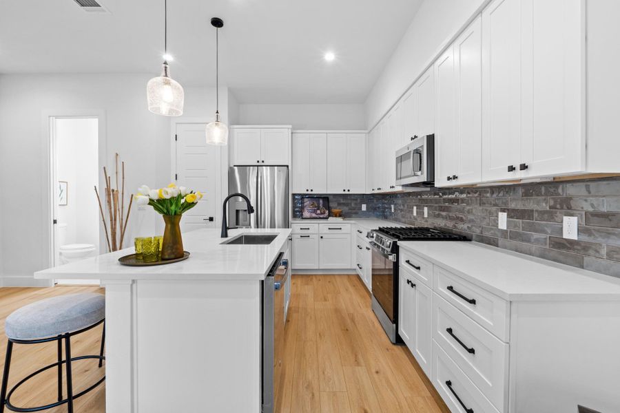 Kitchen featuring stainless steel appliances, white cabinetry, a kitchen island with sink, and hanging light fixtures
