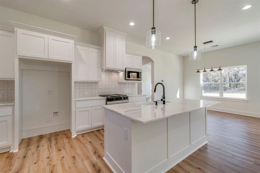 Kitchen with decorative light fixtures, sink, stainless steel appliances, and white cabinetry