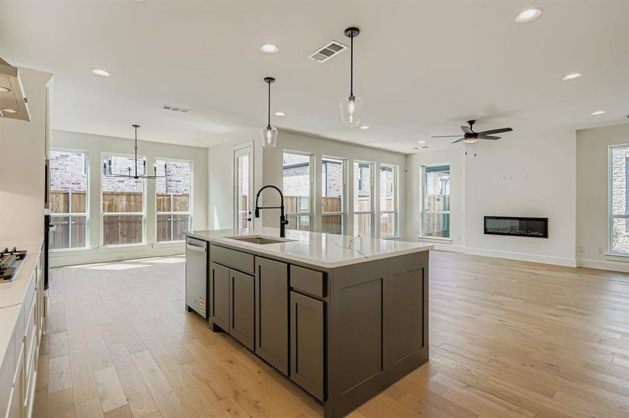 Kitchen featuring hanging light fixtures, open floor plan, a center island with sink, recessed lighting, and light wood-style flooring