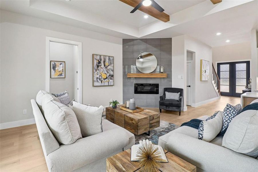 The living room offers hardwood flooring, a modern fireplace with a tiled surround and wooden mantel, and a tray ceiling with exposed wooden beams