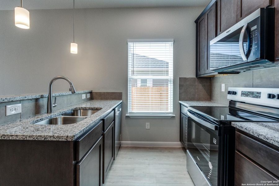 Contemporary kitchen featuring granite countertops, dark wood cabinetry, stainless steel appliances, and wood-finish flooring