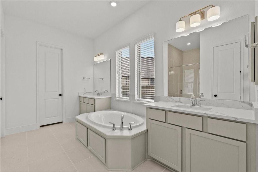 Spa-like en-suite bath with dual vanities, a walk-in shower, soaking tub, and large walk-in closet