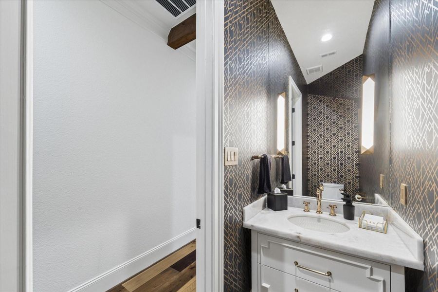 The dramatic powder bath makes a memorable impression with its sophisticated jewel-box design. Full custom wallpaper surrounds the space with rich pattern and dimension, while a floating custom vanity topped with marble adds modern elegance. A full-height mirror extending toward the ceiling, designer sconces, and thoughtfully coordinated finishes create a refined guest experience. Every element reflects the home’s commitment to distinctive materials and elevated craftsmanship.