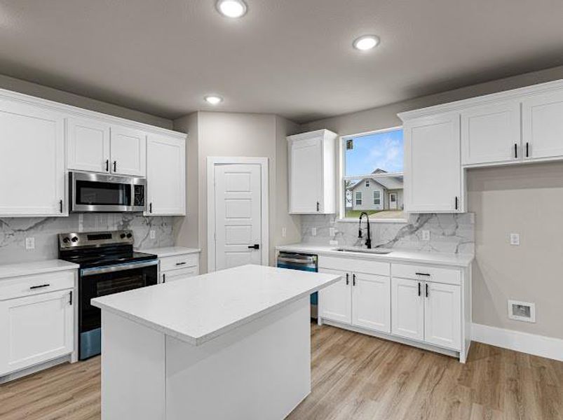 Kitchen featuring appliances with stainless steel finishes, white cabinets, light wood finished floors, a kitchen island, and tasteful backsplash Kitchen featuring appliances with stainless steel finishes, white cabinets, light wood finished floors, a kitchen island, and tasteful backsplash