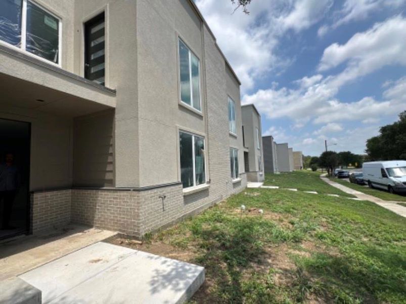 View of side of property featuring brick siding, stucco siding, a patio area, a lawn, and a residential view View of side of property featuring brick siding, stucco siding, a patio area, a lawn, and a residential view