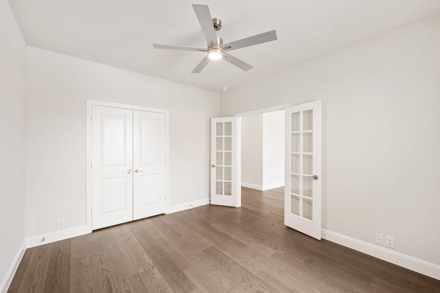 Empty bedroom with hardwood floors, ceiling fan, double closet, and French doors leading to adjoining room