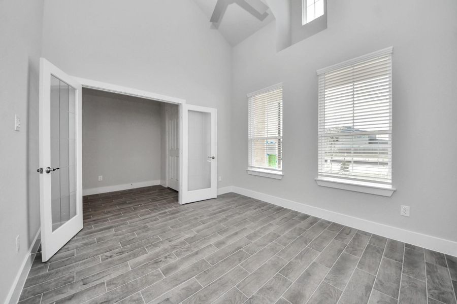 Experience the perfect blend of sophistication and warmth in this home office, boasting elegant wood-look tile flooring and flooded with natural light from expansive windows and French doors.