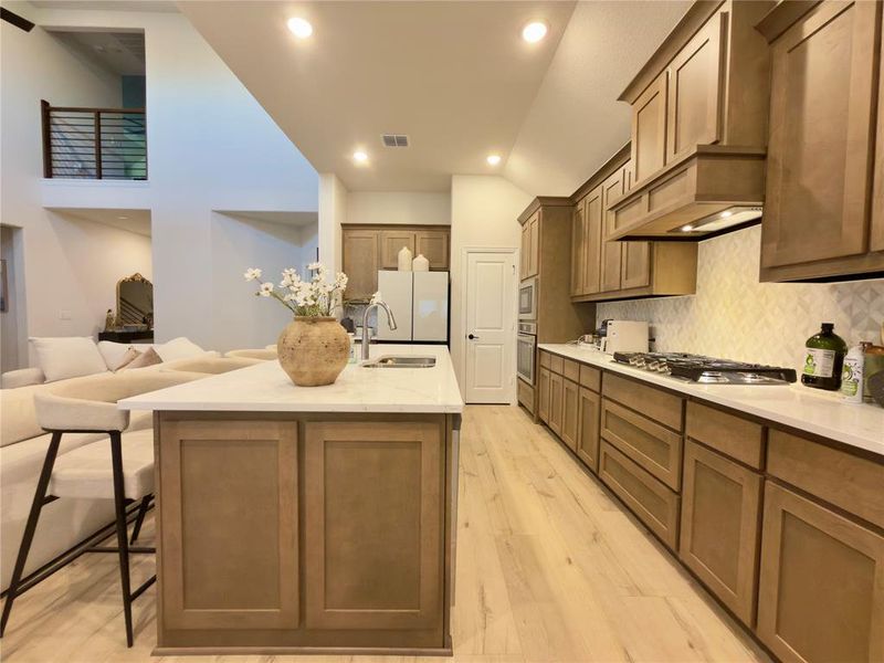Kitchen with light stone countertops, a center island with sink, light wood-style flooring, stainless steel appliances, and a kitchen bar