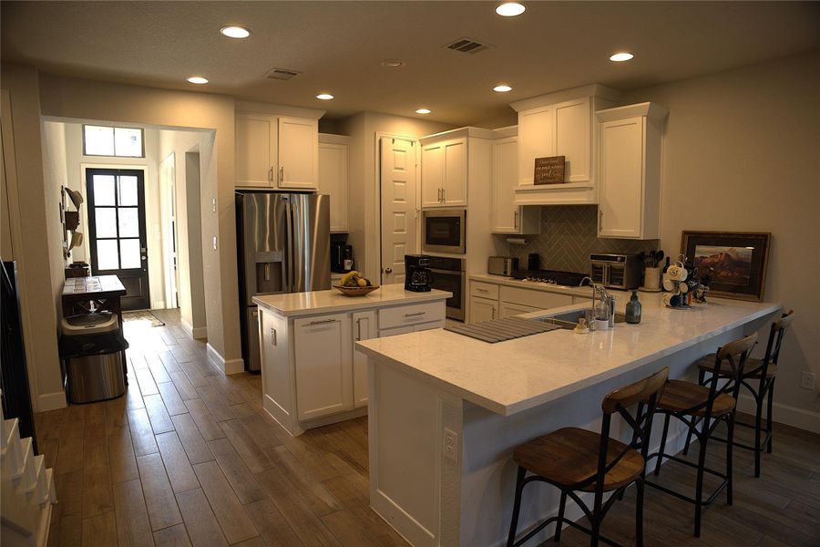 Kitchen with white cabinets, a peninsula, black appliances, a breakfast bar, and a center island Kitchen with white cabinets, a peninsula, black appliances, a breakfast bar, and a center island
