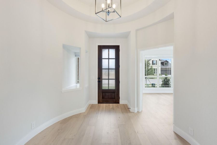 Bright home entryway with tray ceiling, chandelier, dark wood front door, and light hardwood floors Bright home entryway with tray ceiling, chandelier, dark wood front door, and light hardwood floors