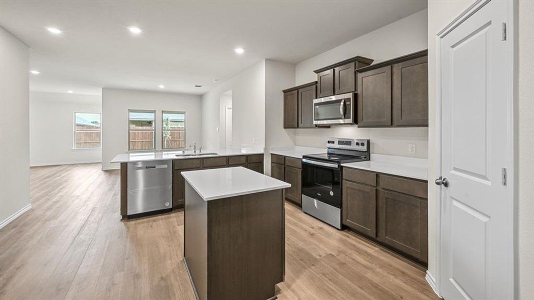 Kitchen with stainless steel appliances, light countertops, dark wood finish cabinetry, a peninsula, and a center island