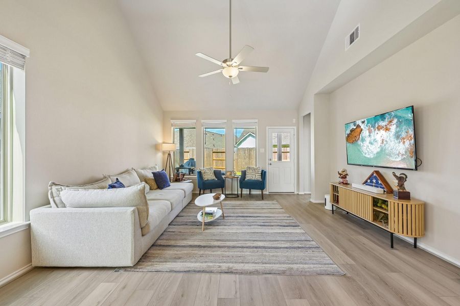 Spacious living room with vaulted ceilings, abundant natural light, and modern finishes. Features a comfortable seating area, stylish media console, and access to a cozy outdoor space.