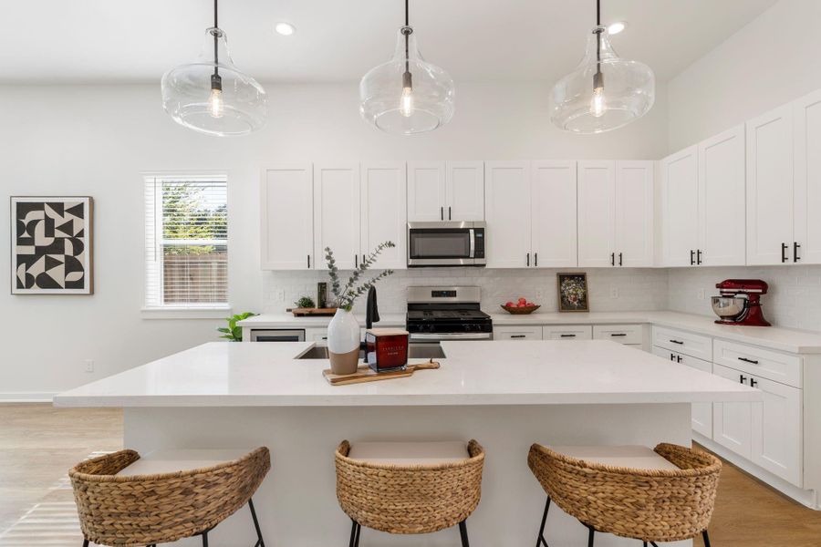 Kitchen island seating Quartz Carrara countertops, a farmhouse sink, timeless white subway tile backsplash, all highlighted by matte black finishes.