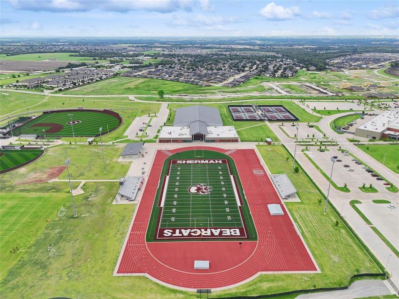 Aerial perspective showcasing a large sports complex featuring a football field with track, multiple baseball diamonds, and tennis courts
